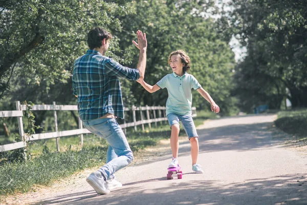 Dark-haired boy riding a skateboard and giving high five to his dad — Stock Photo, Image
