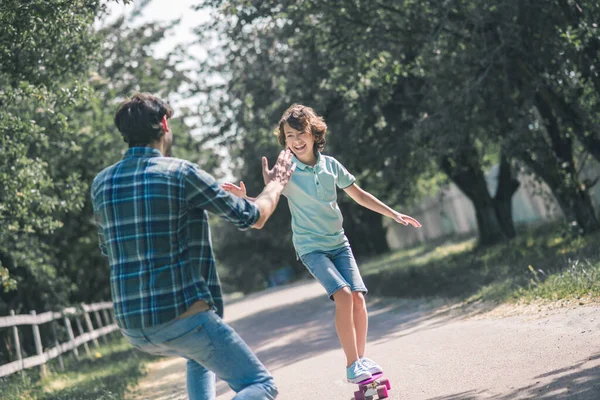 Mörkhårig pojke åker skateboard, hans pappa fångar honom — Stockfoto