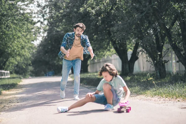 Ragazzo dai capelli scuri che cade a terra, suo padre che corre ad aiutarlo — Foto Stock