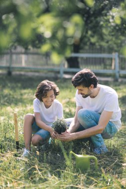 Koyu saçlı çocuk ve babası bitkiyi tutuyorlar ve gülümsüyorlar.