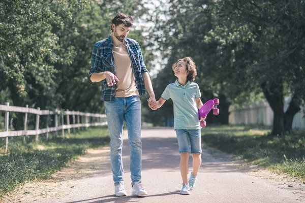 Niño moreno con un monopatín y su padre caminando por el parque —  Fotos de Stock