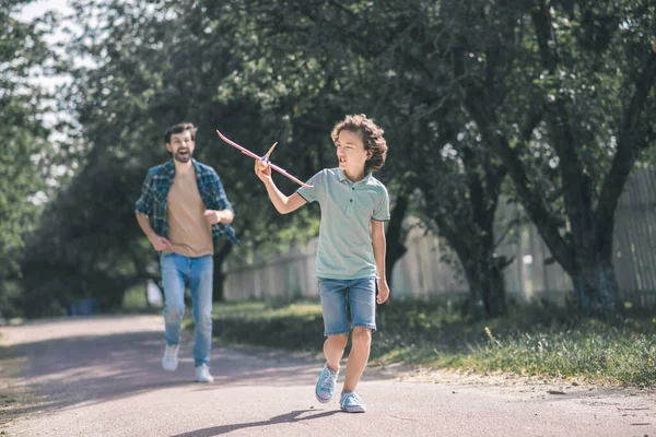 Dunkelhaariger Junge rennt mit Spielzeugflugzeug, sein Vater rennt ihm hinterher — Stockfoto