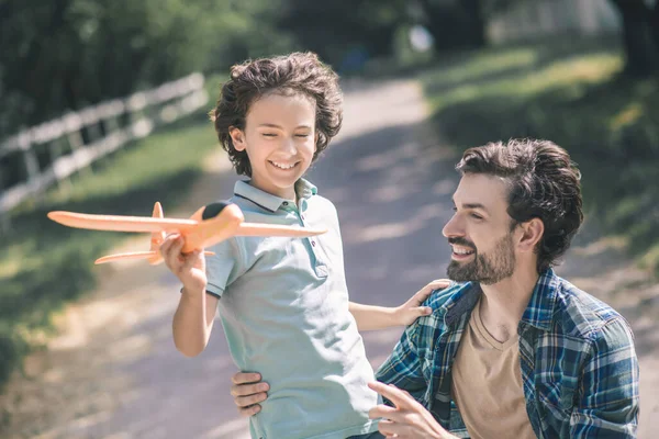 Happy dark-haired boy holding a toy plane and touching his fathers shoulder