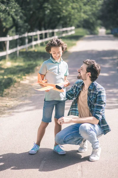 Niño moreno sosteniendo un avión de juguete y sintiéndose emocionado, padre sintiéndose feliz — Foto de Stock