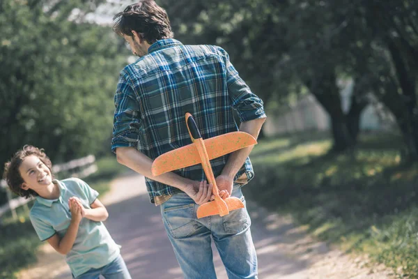 Vater hält ein Spielzeugflugzeug hinter seinem Rücken, ein Junge ist aufgeregt — Stockfoto