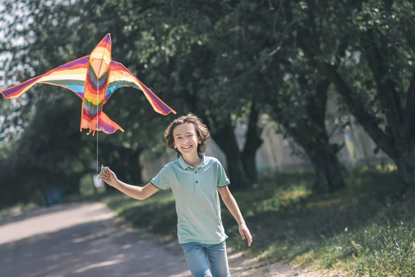 Niño moreno sosteniendo una cometa colorida y luciendo feliz — Foto de Stock