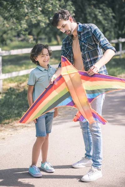 Hombre de pelo oscuro sosteniendo una cometa de colores y explicando a su hijo cómo usarlo —  Fotos de Stock