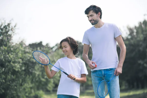 Siyah saçlı çocuk elinde badminton raketi tutuyor ve babasıyla oynamaya hazır. — Stok fotoğraf