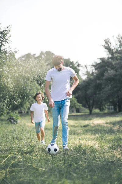 Ciemnowłosy chłopiec i jego ojciec bawią się piłką w ogrodzie — Zdjęcie stockowe