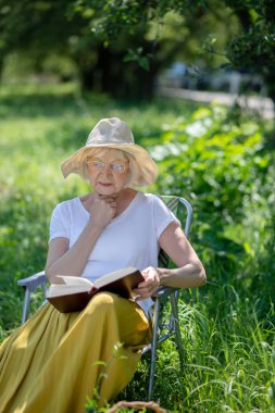 Açık havada kitap okuyan düşünceli yaşlı kadın.