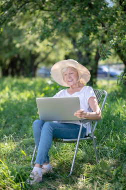 Bahçesinde dizüstü bilgisayarla çalışan yaşlı bir kadın.