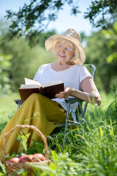 Улыбающаяся пожилая женщина наслаждается чтением книги в саду — стоковое фото