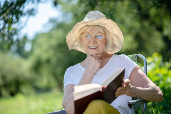 Opgewonden oudere vrouw die een interessant boek leest — Stockfoto