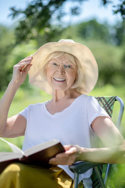 Mulher sorridente usando um chapéu e segurando um livro — Fotografia de Stock