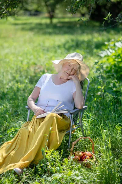 Oudere vrouw slaapt in de ligstoel met een boek — Stockfoto