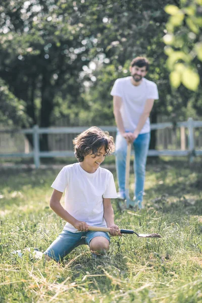 Niño de pelo oscuro y su padre buscando ocupado con la jardinería — Foto de Stock