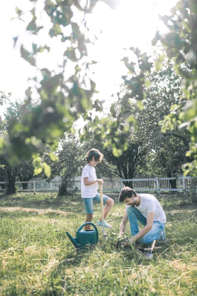 Niño de pelo oscuro y su padre se ven ocupados mientras trabajan en el jardín — Foto de Stock