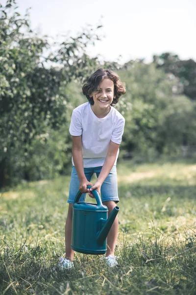 Sötét hajú fiú, kezében az öntözőkannával és mosolyog. — Stock Fotó