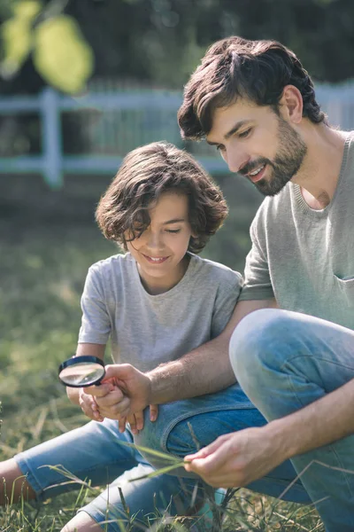 虫眼鏡を通して植物を見ている彼の父と暗い髪の男の子と興味を持って見て — ストック写真