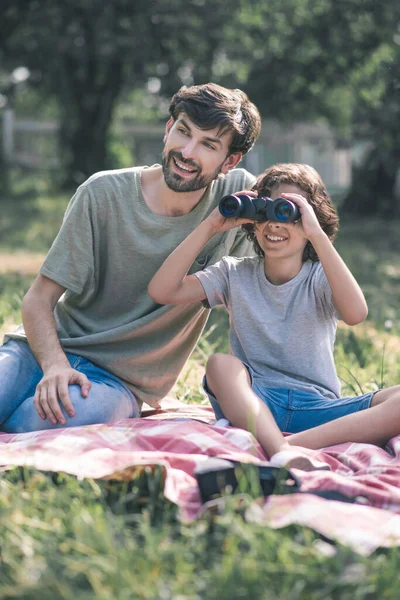 Niño moreno sentado junto a su padre viendo prismáticos, mirando interesado — Foto de Stock