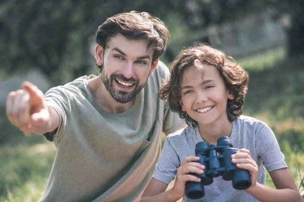 黒髪の男の子は双眼鏡を持っていて、父親は何かを見せている。 — ストック写真