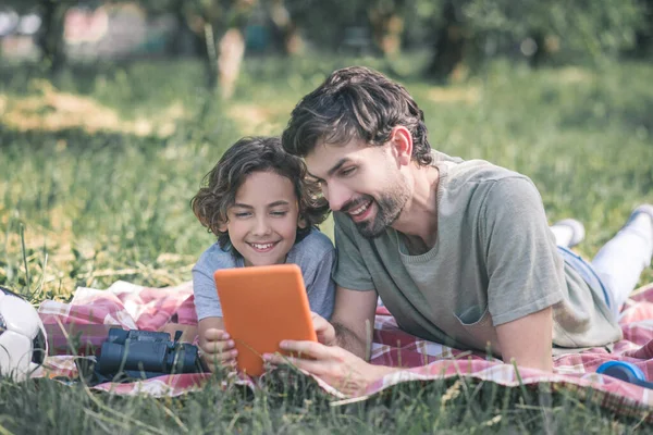 Papá e hijo viendo algo en la tableta y sonriendo — Foto de Stock