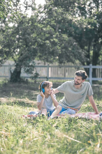 Smiling son sitting near his dad and listening to music — Stock Photo, Image