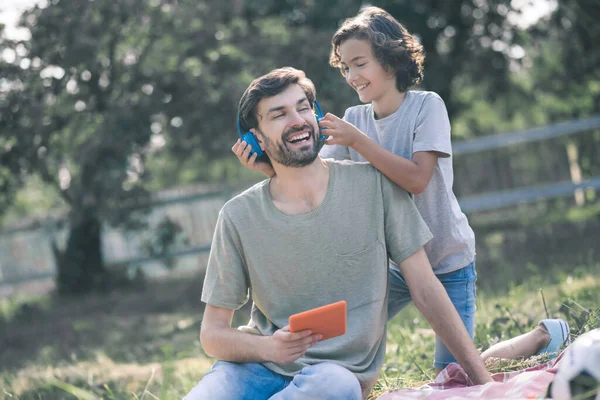 Smiling son putting earphones on his fathers head, both feeling good