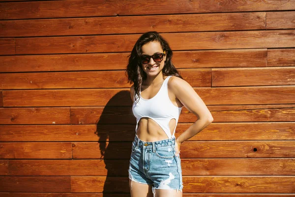 Bella ragazza bruna in pantaloncini in piedi vicino al muro di legno — Foto Stock
