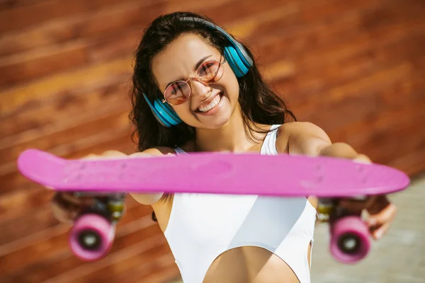 Krásná brunetka dívka ukazuje skateboard a usmívá — Stock fotografie