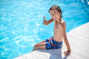 Çocuk havuz kenarında oturmuş el kol hareketi yapıyor.