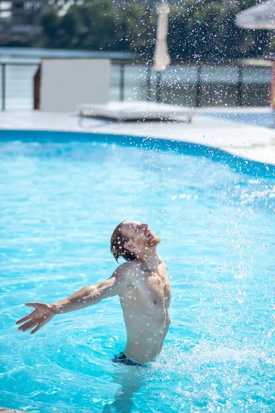 Joyful man with open arms in water in pool