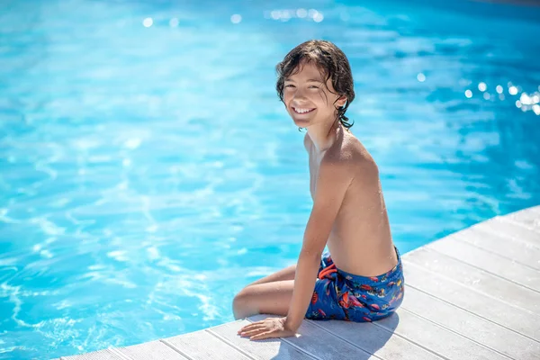 Garoto sorridente sentado na beira da piscina alegremente — Fotografia de Stock
