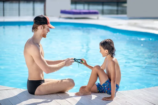 Homem e menino sentados em frente uns dos outros perto da piscina — Fotografia de Stock