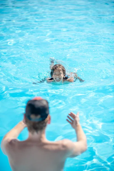 Man with back and boy swimming towards him — Stock Photo, Image