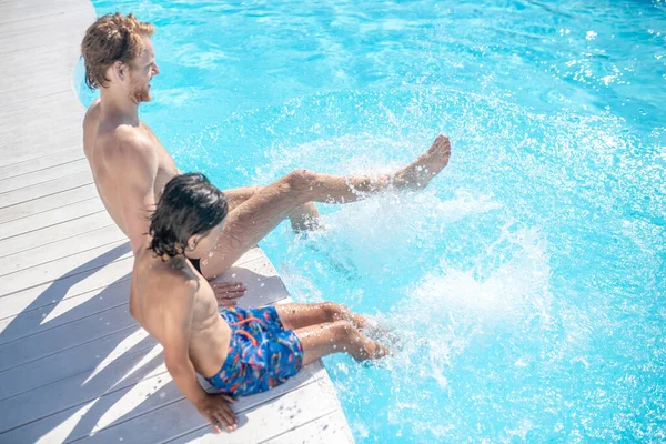 Pai e filho movendo as pernas na água da piscina — Fotografia de Stock