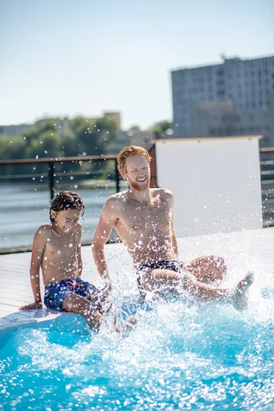 Pai alegre com filho fazendo salpicos na piscina — Fotografia de Stock