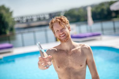 Kızıl saçlı adam elinde bir şişe içme suyu tutuyor..