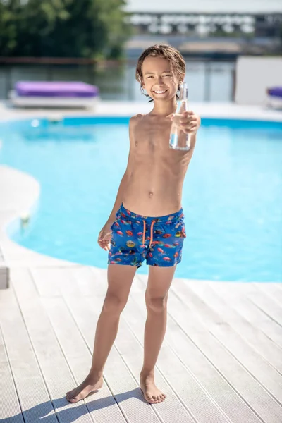 Menino em shorts com garrafa de água perto da piscina — Fotografia de Stock