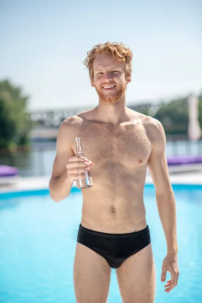 Muskularny mężczyzna z butelką wody stojącej przy basenie — Zdjęcie stockowe