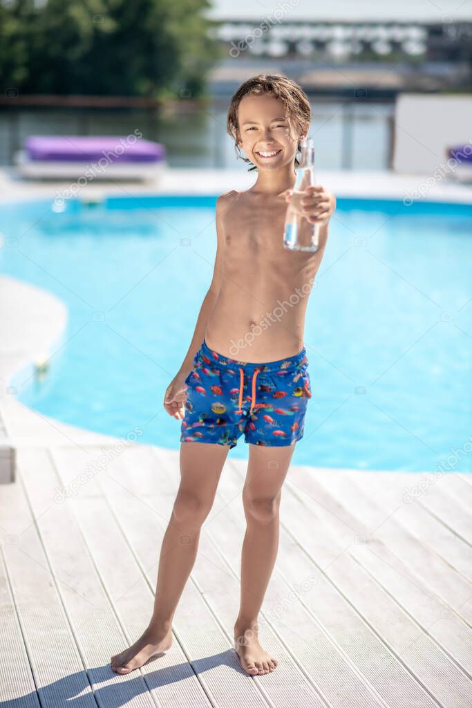 Boy in shorts with bottle of water near pool