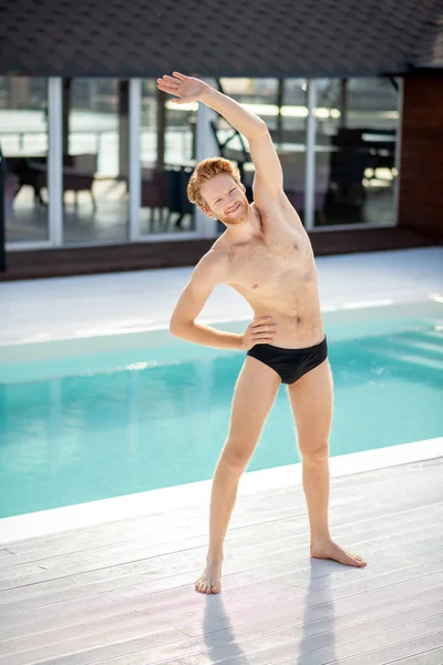 Havuzun kenarına yaslanmış gülümseyen genç adam — Stok fotoğraf