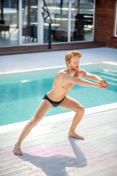 Vážný mladý vousatý chlap cvičení v blízkosti bazénu — Stock fotografie