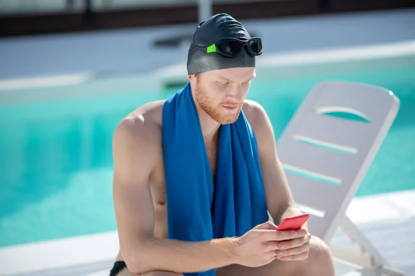 Atento nadador masculino com smartphone sentado à beira da piscina — Fotografia de Stock