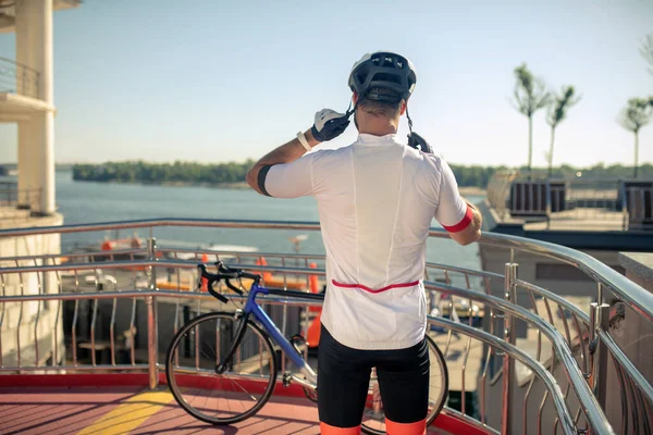 Man putting bicycle helmet standing with his back