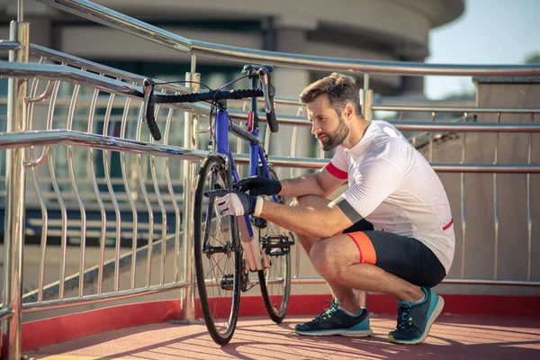 Красивый молодой человек в спортивной одежде осматривает велосипед — стоковое фото
