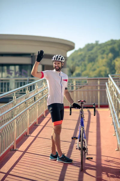 Улыбающийся велосипедист, стоящий с поднятой рукой — стоковое фото