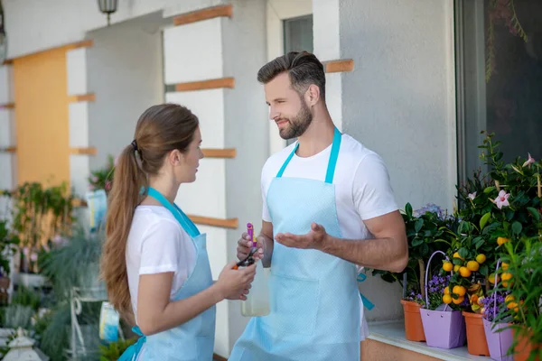 Varón barbudo y hembra de cabello castaño de pie fuera de la florería, hablando — Foto de Stock