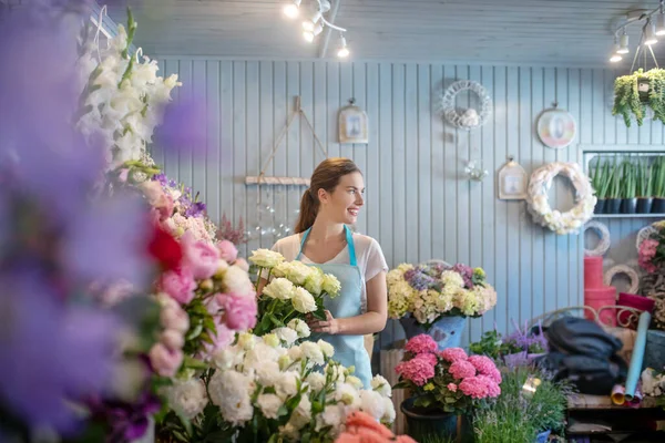 Femenino de cabello castaño parado en el soporte de flores, tocando rosas blancas, mirando hacia los lados — Foto de Stock