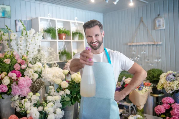 Sonriente barbudo rociando agua masculina en la cámara dentro de la florería —  Fotos de Stock